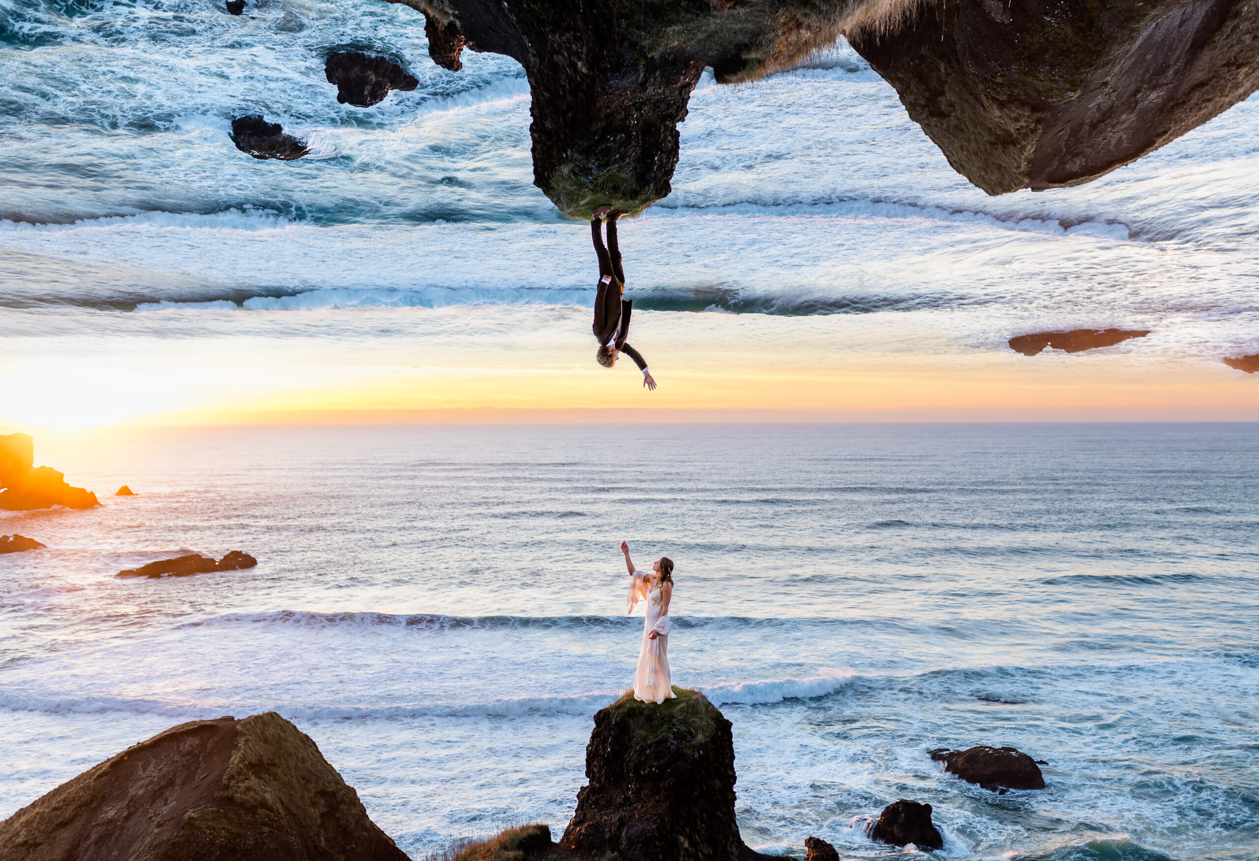 A surreal and artistic elopement on the Oregon Coast featuring a double-exposure effect. A bride stands on a rocky cliffside, reaching toward her groom, who appears upside down in a dreamy, mirrored ocean sky. The backdrop of crashing waves, golden sunset light, and dramatic coastal cliffs enhances the ethereal and adventurous feel of this unique elopement photography.